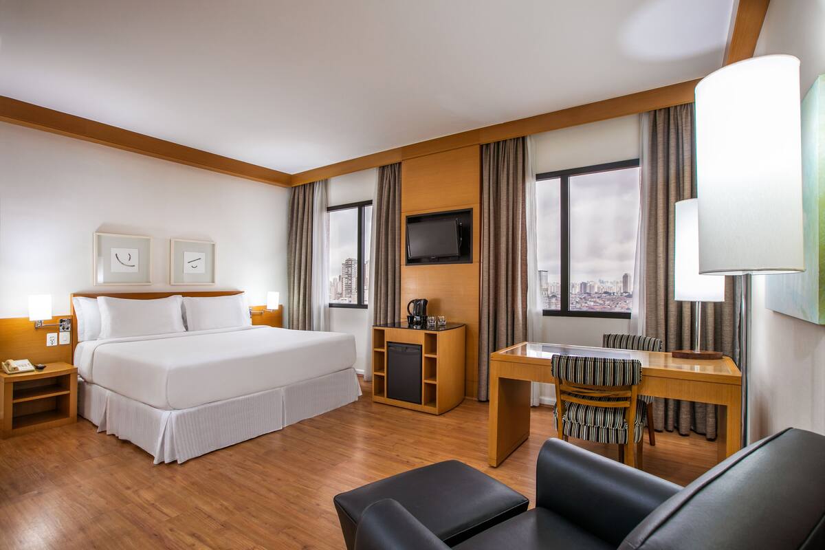 Habitación de hotel con cama, escritorio, silla, televisión y vista a la ciudad.