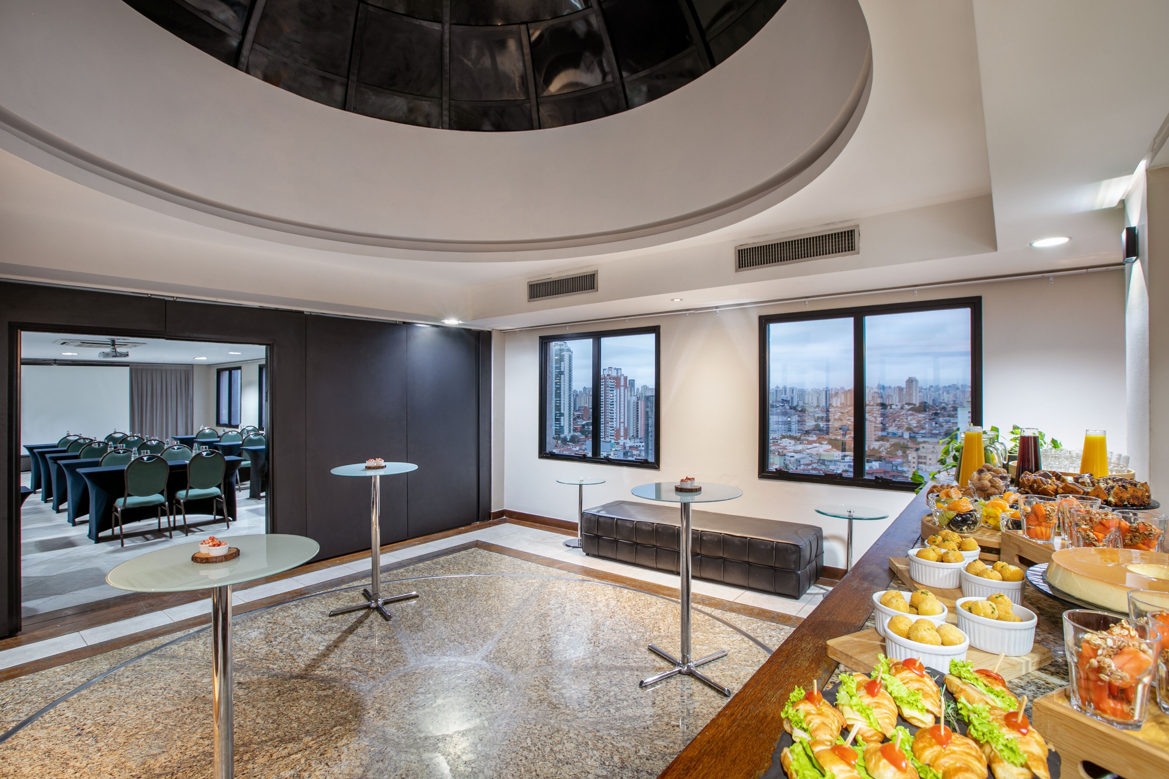 A spacious conference room with a panoramic city view, a buffet with various food items, and a seating area with a sofa.