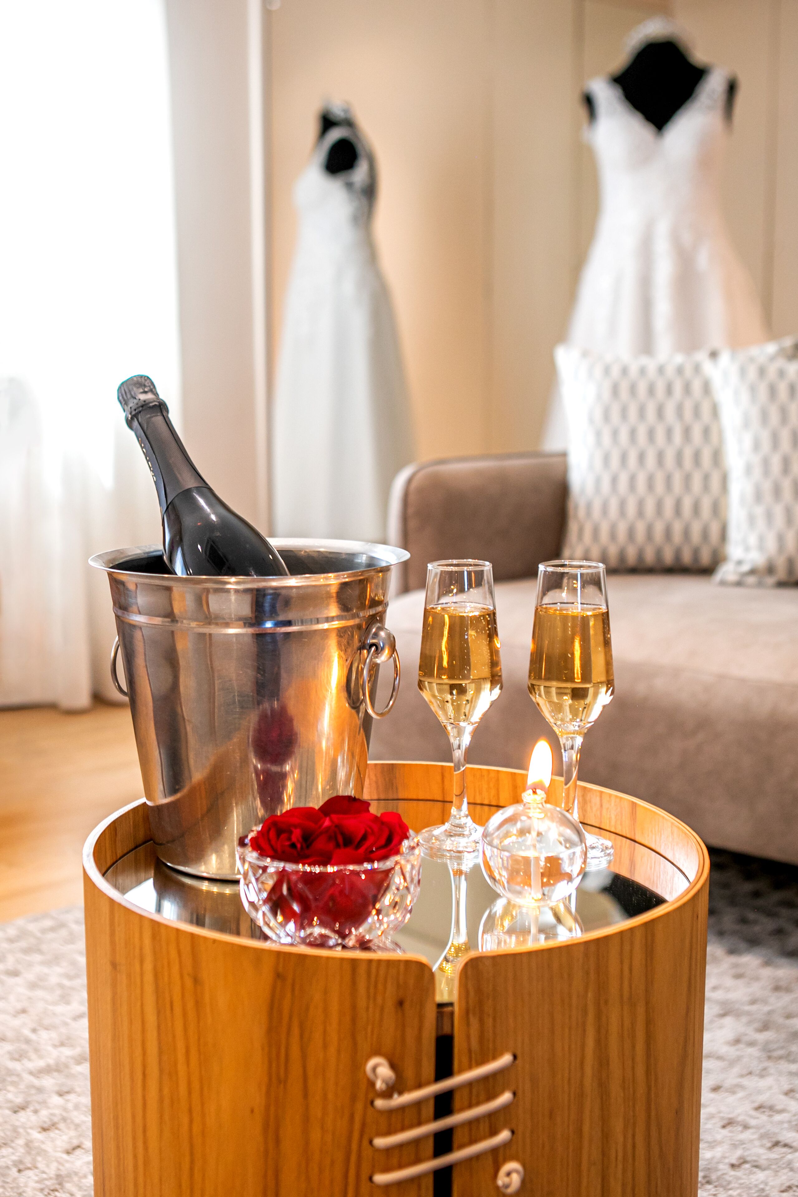 A wooden tray with a champagne bottle, two glasses, and a bowl of red roses.