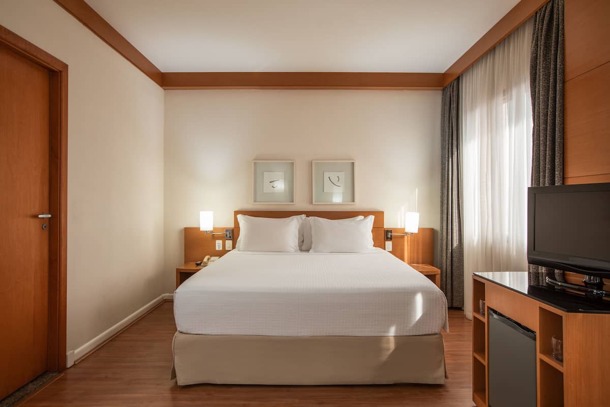 Una habitación de hotel con una cama grande, lámparas de noche, un televisor y un armario de madera.