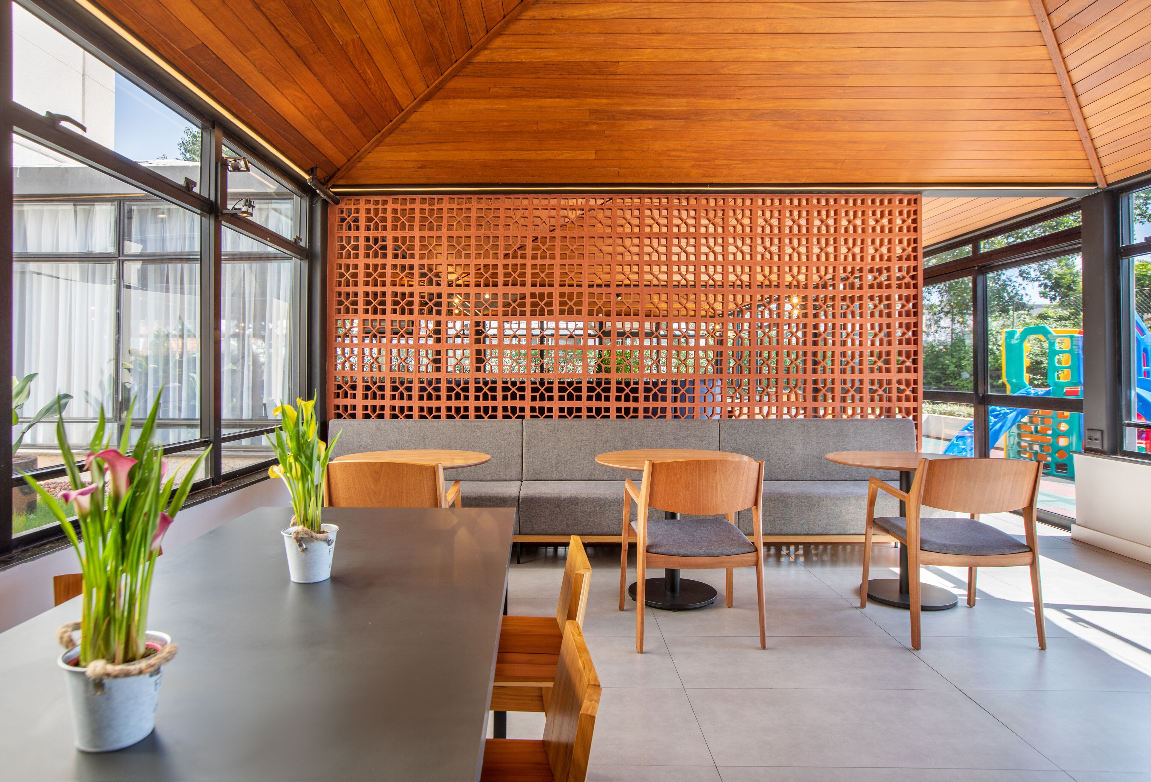 A modern indoor seating area with wooden tables and chairs, a grey sofa, and a decorative wooden lattice wall.