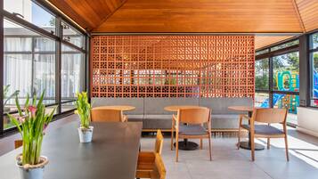A modern indoor seating area with wooden tables and chairs, a grey sofa, and a decorative wooden lattice wall.