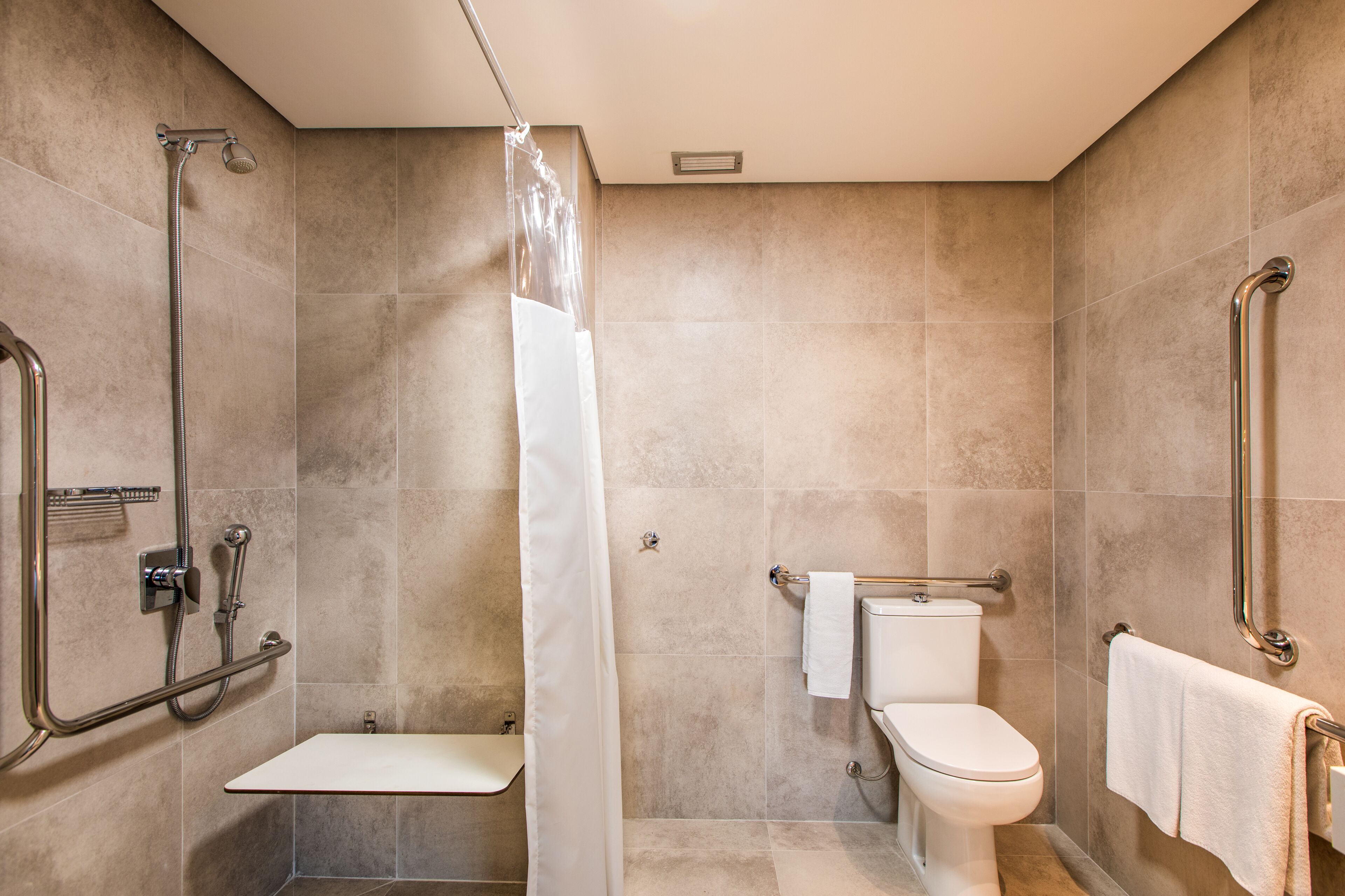 Un baño con ducha, inodoro y barras de apoyo.