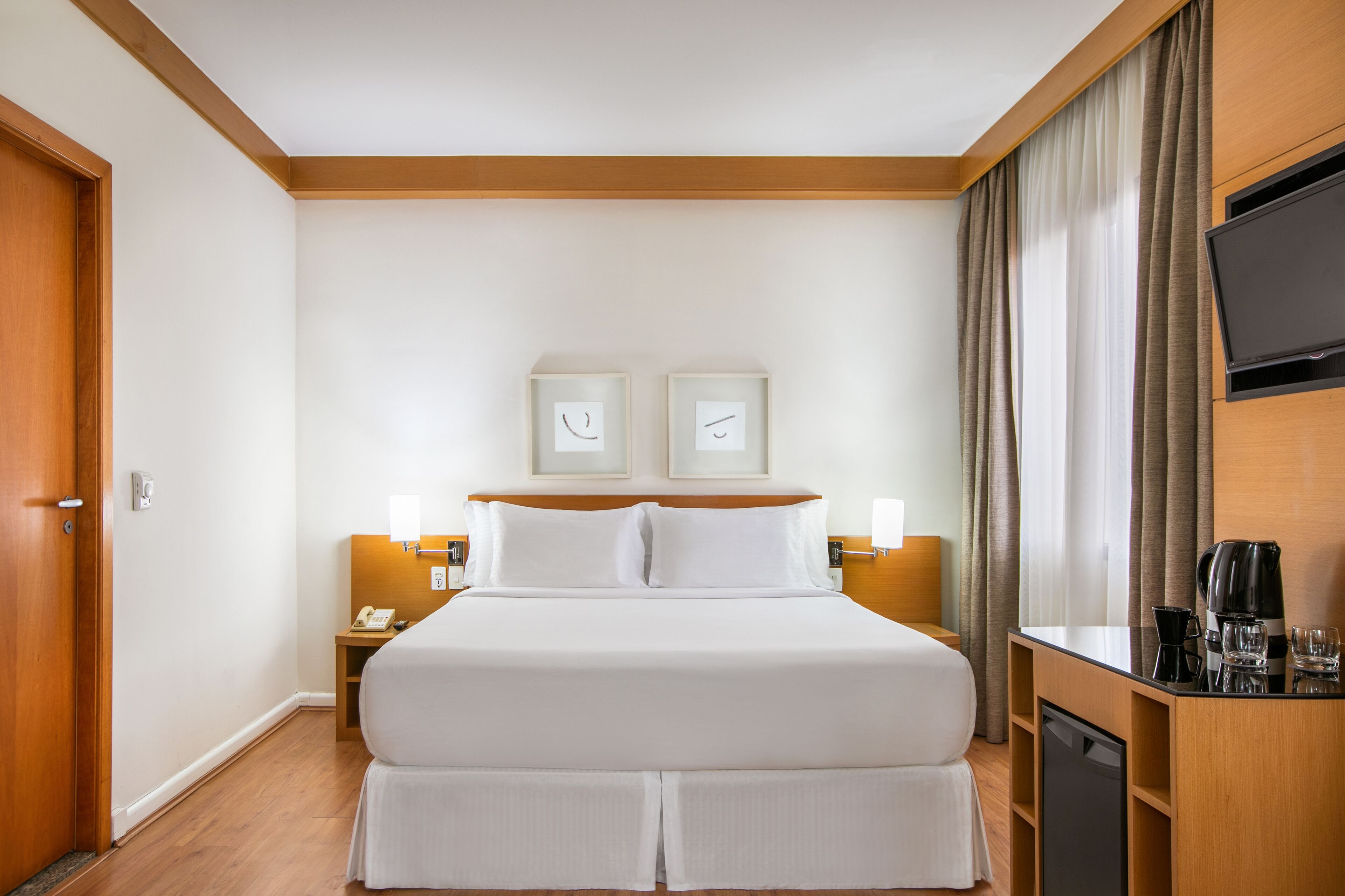 Una habitación de hotel con una cama grande, mesitas de noche con lámparas, un televisor de pantalla plana y una cafetera.