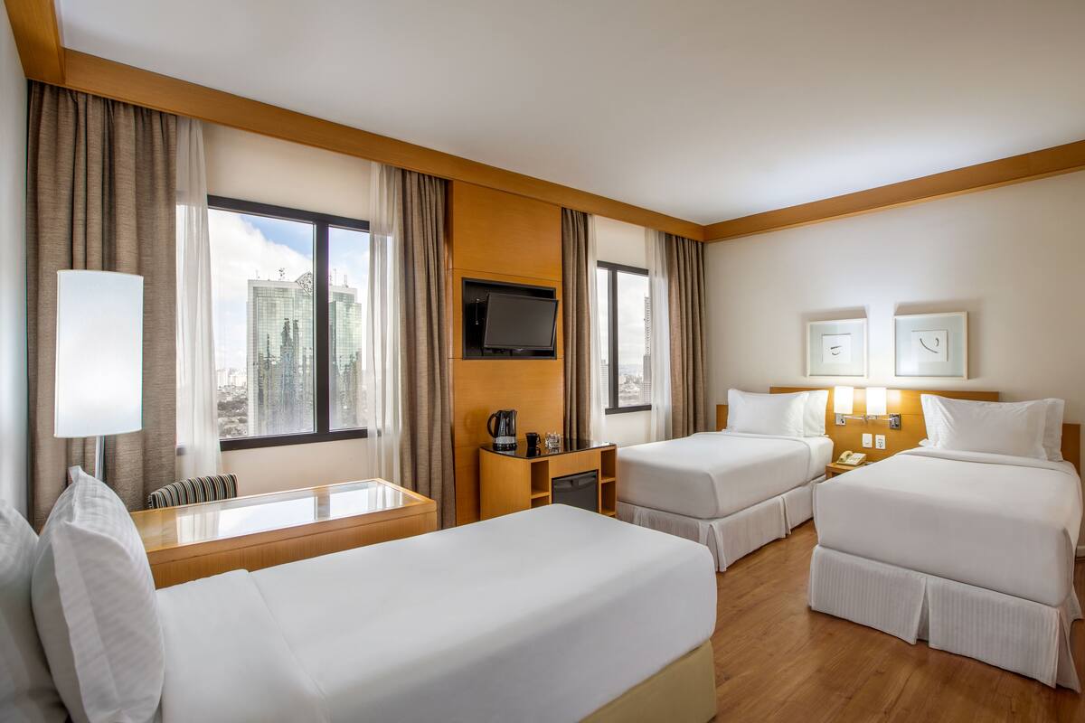 Habitación de hotel con dos camas, televisión, escritorio con lámpara y vista a la ciudad.