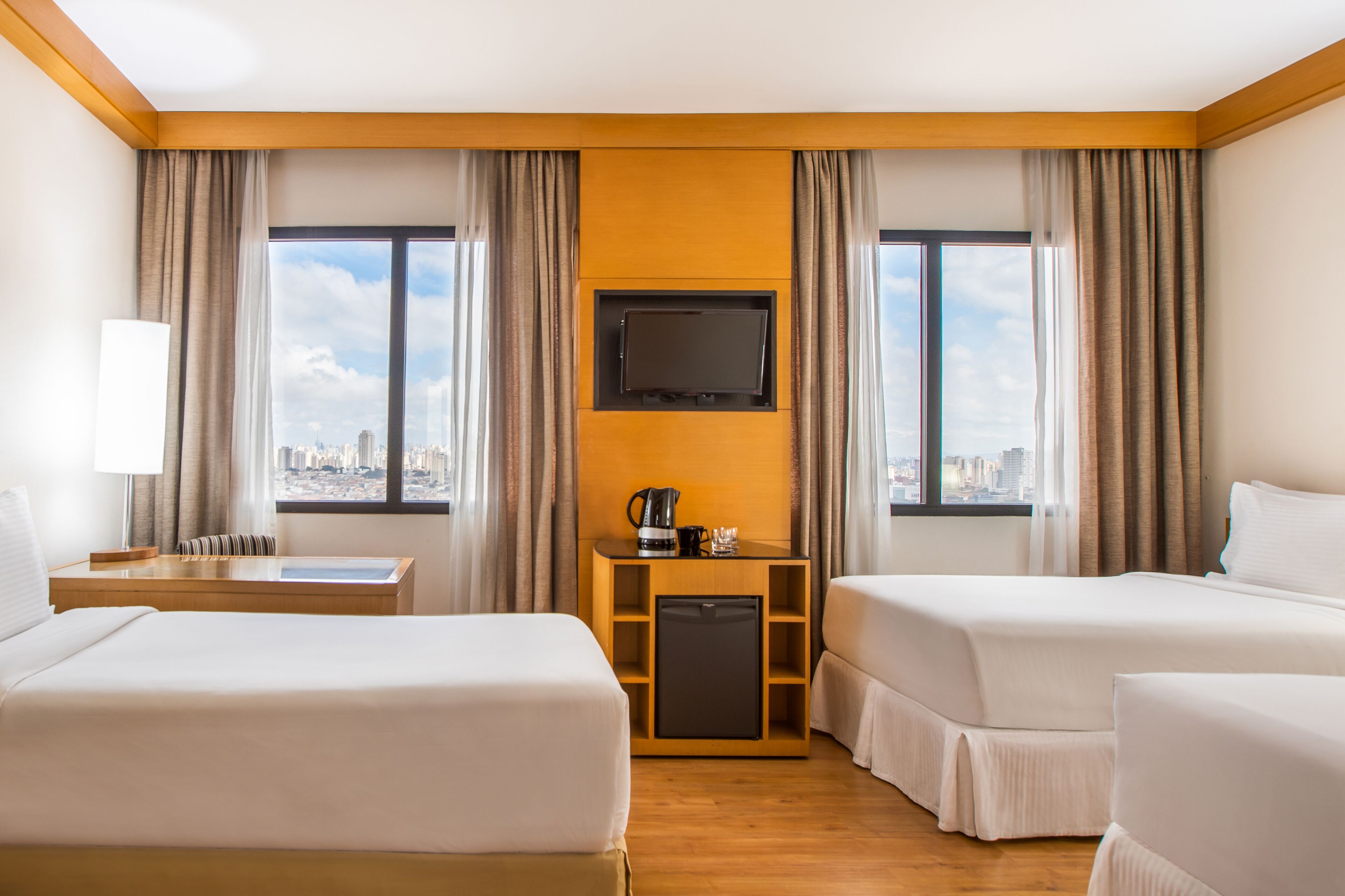 A hotel room with two beds, a TV, a coffee maker, and a city view.