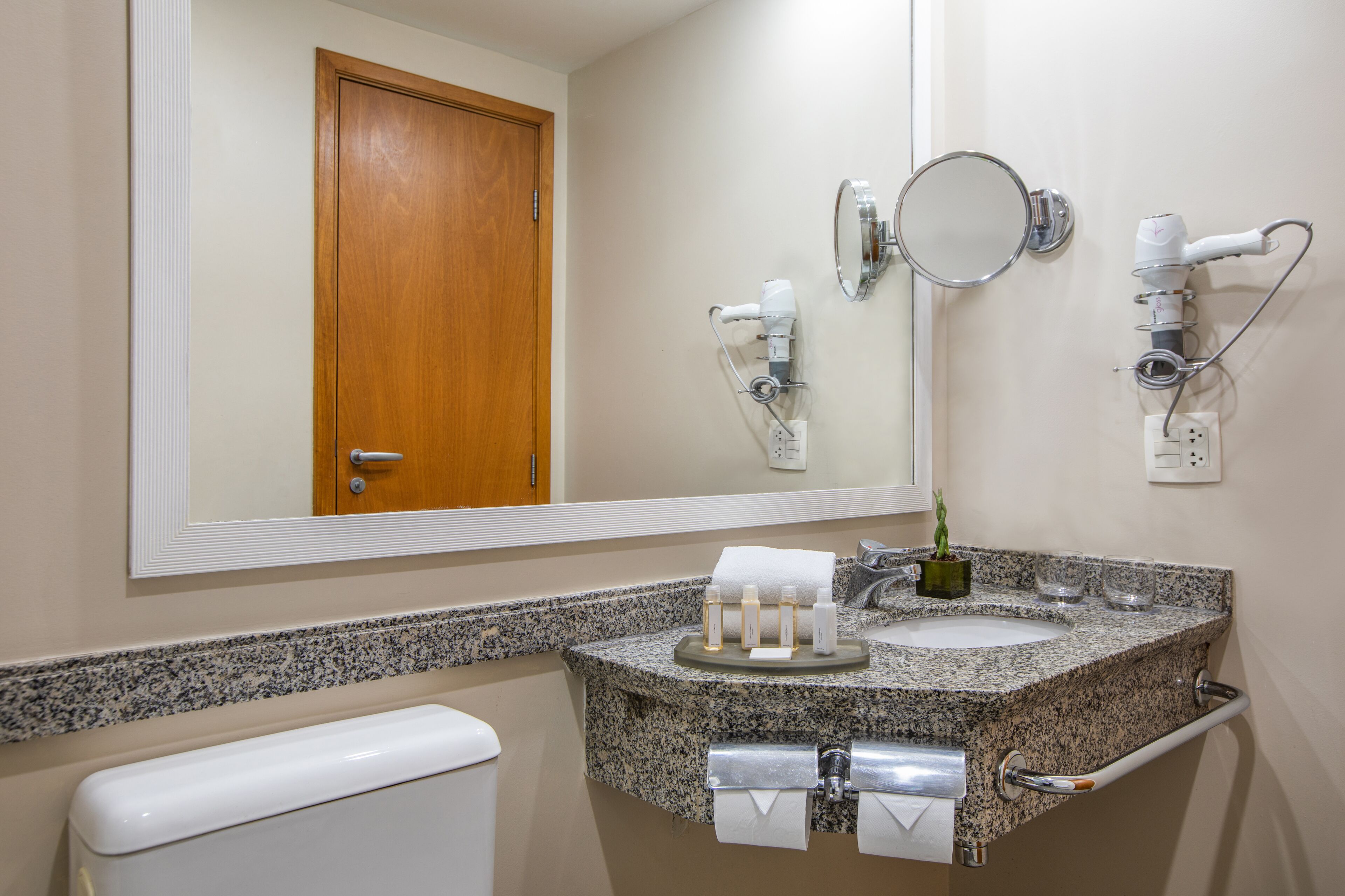 A bathroom with a granite countertop, a sink, a mirror, a towel rack, and a hairdryer.