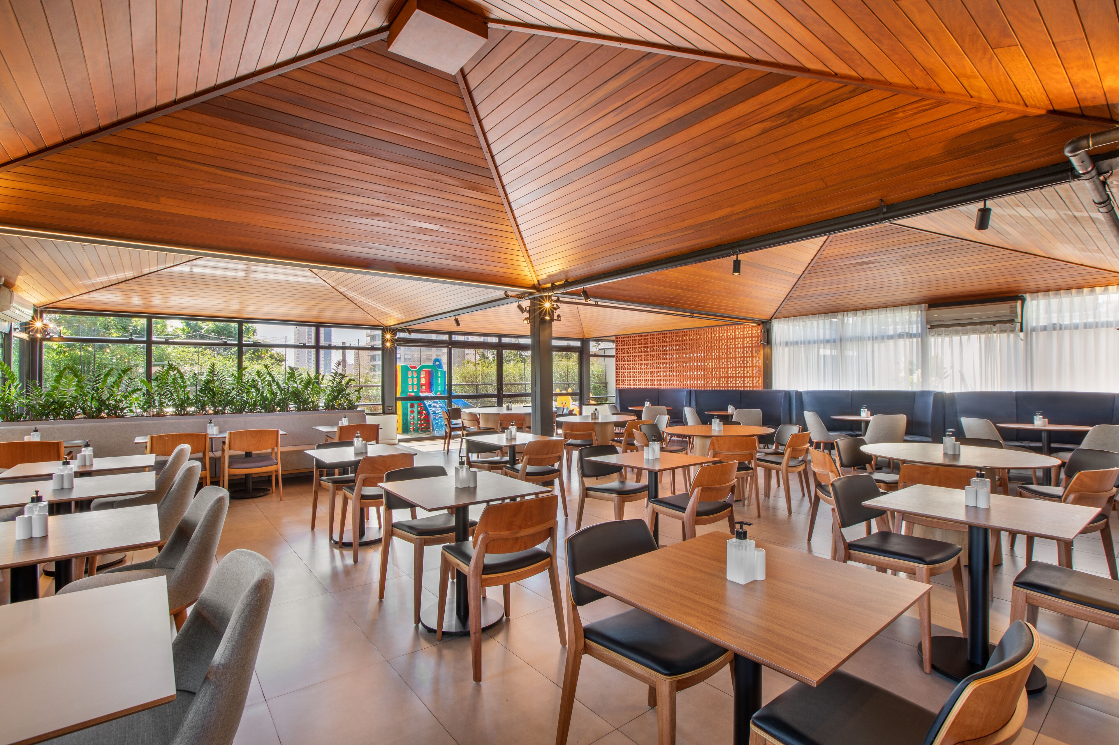 A spacious indoor dining area with wooden tables and chairs, large windows, and a high ceiling.