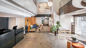 Un vestíbulo moderno con mostrador de recepción, zona de estar, escalera y ventanas amplias.