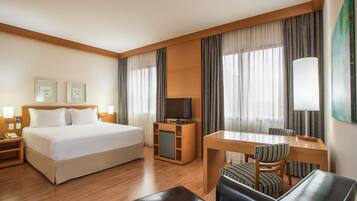 A hotel room with a bed, a desk with a chair, a TV, and a lamp.