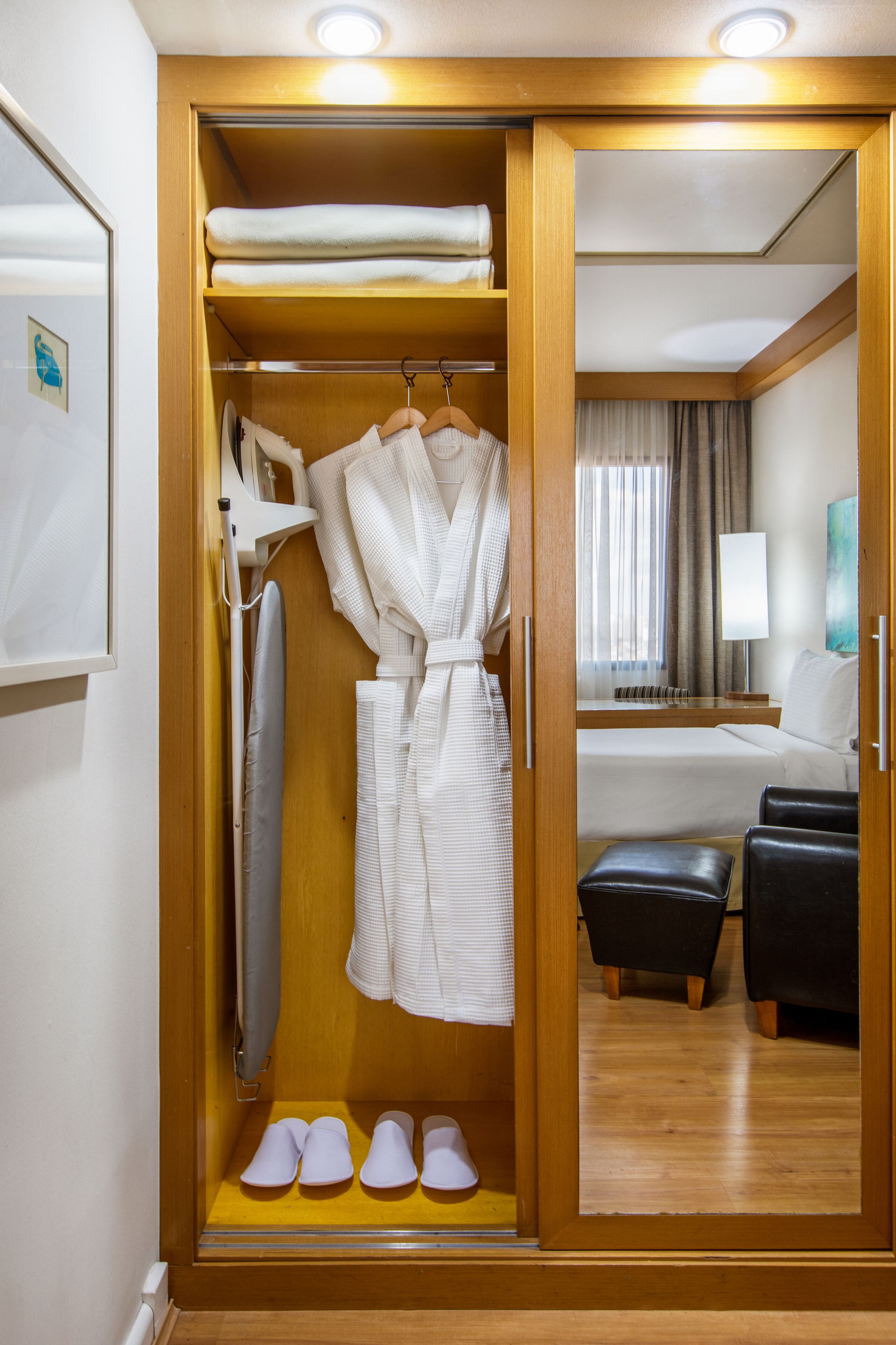 A hotel room with a walk-in closet containing a robe, slippers, and a hanging garment.
