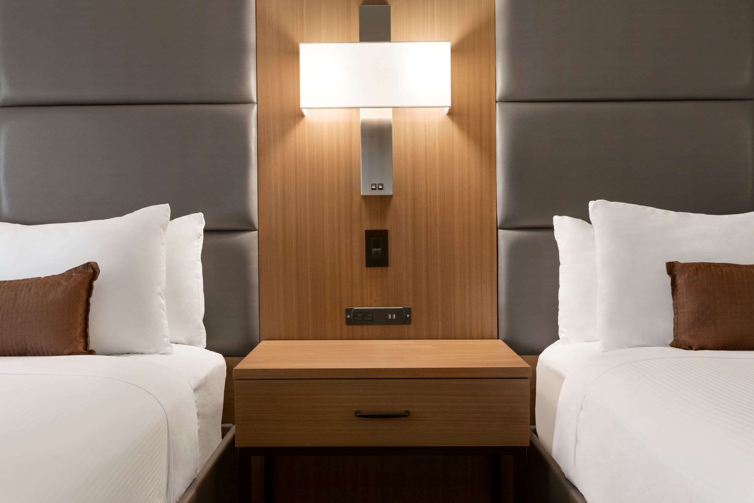 Ein Hotelzimmer mit zwei Betten, einem hölzernen Nachttisch mit Schublade und einer Wandleuchte.