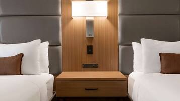 A hotel room with two beds, a wooden nightstand with a drawer, and a wall-mounted light fixture.