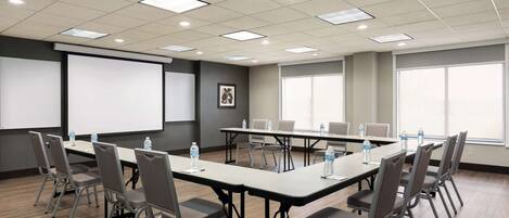 A conference room with a long table, chairs, a projector screen, and large windows.