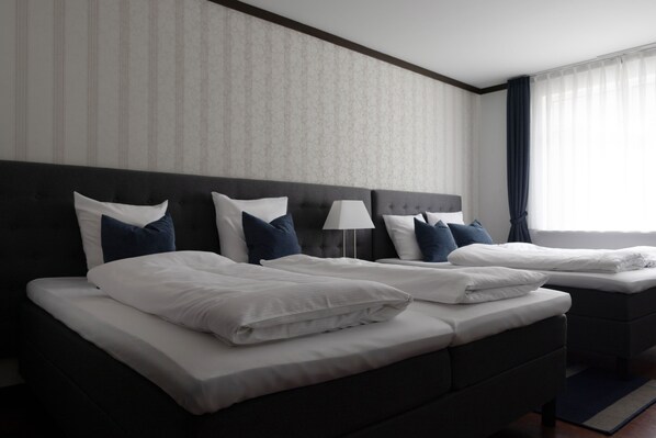A hotel room with two beds, a large window with curtains, and a patterned wall. - Hotel Phønix (Aalborg)