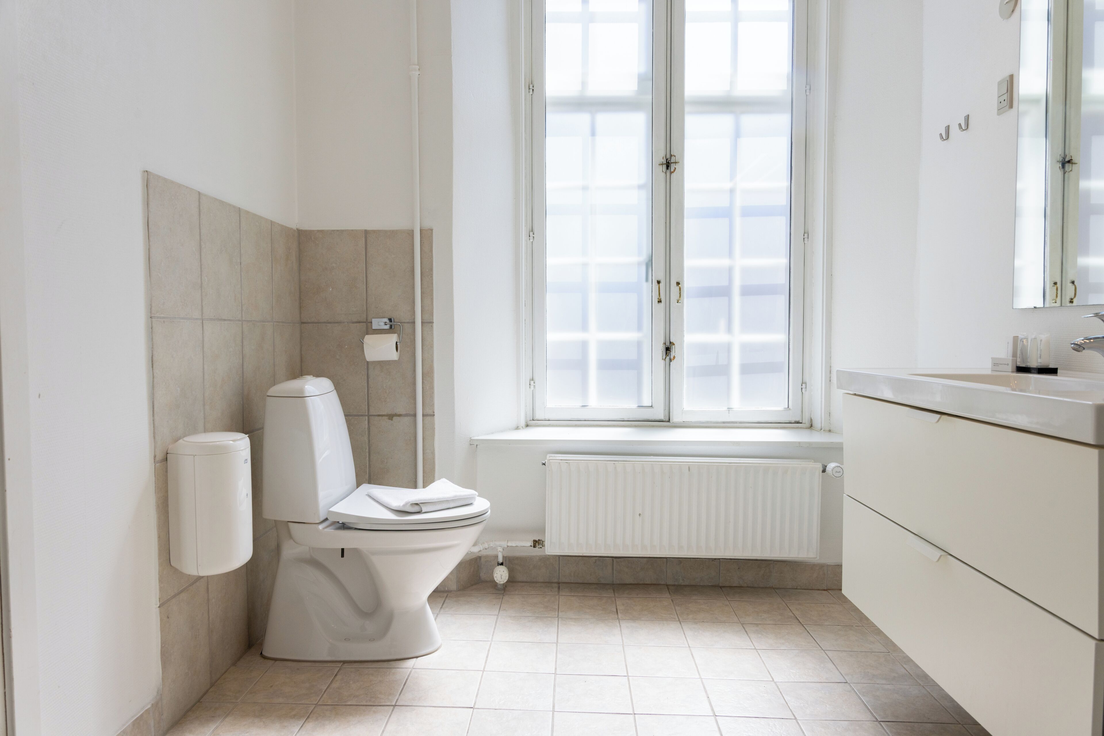 Et moderne badeværelse med toilet, håndtørrer, vindue og radiator.