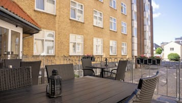 Un área de comedor al aire libre con una mesa y sillas, un farol y vistas de un edificio de ladrillo con ventanas.