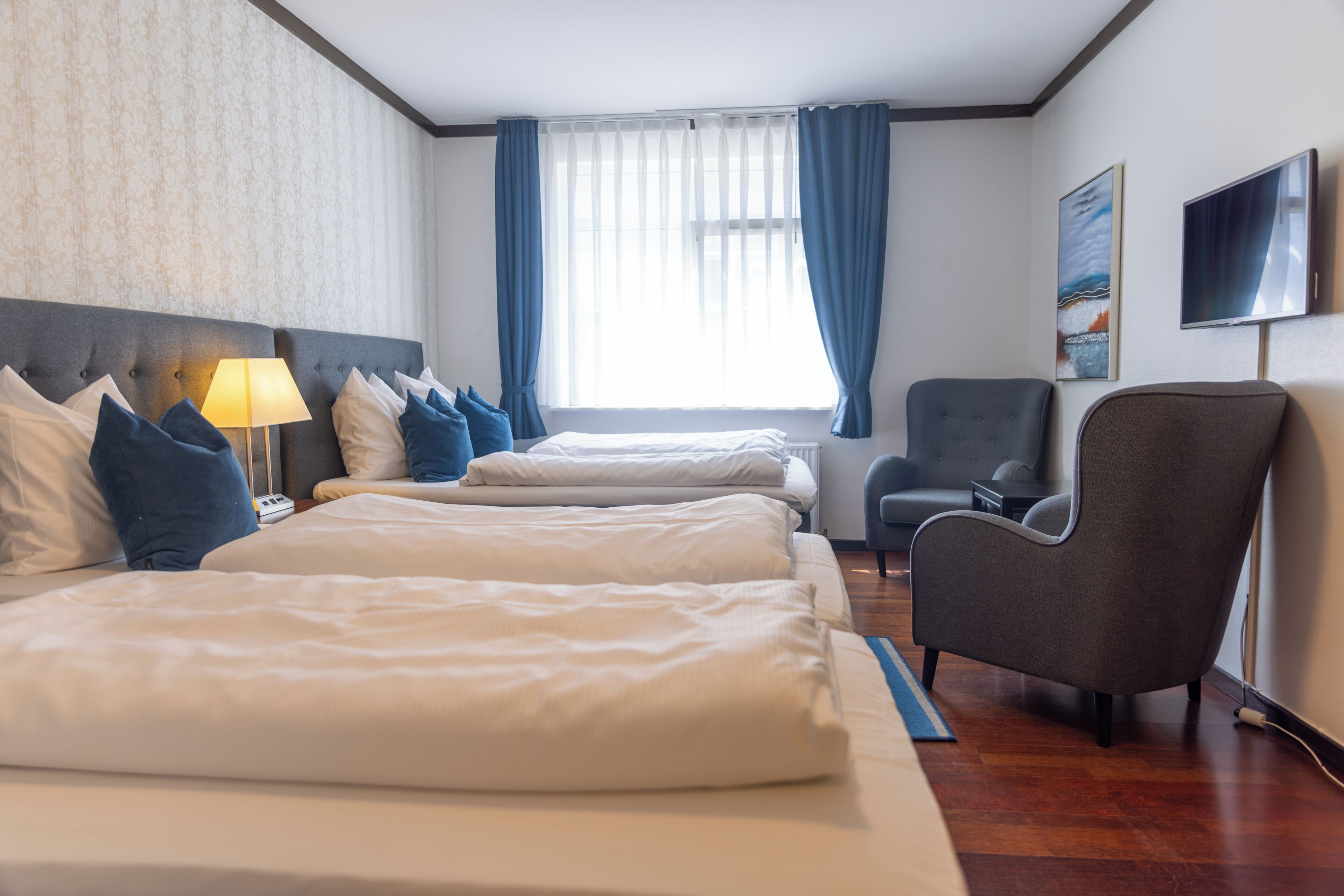 Hotellihuone, jossa on kaksi sänkyä, tuoli, televisio ja ikkuna, jossa on verhot.