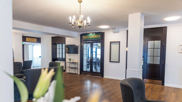 A modern interior with a chandelier, a sign reading 'BRIGADÉREN,' and a door leading to a dining area. - Hotel Phønix (Aalborg)