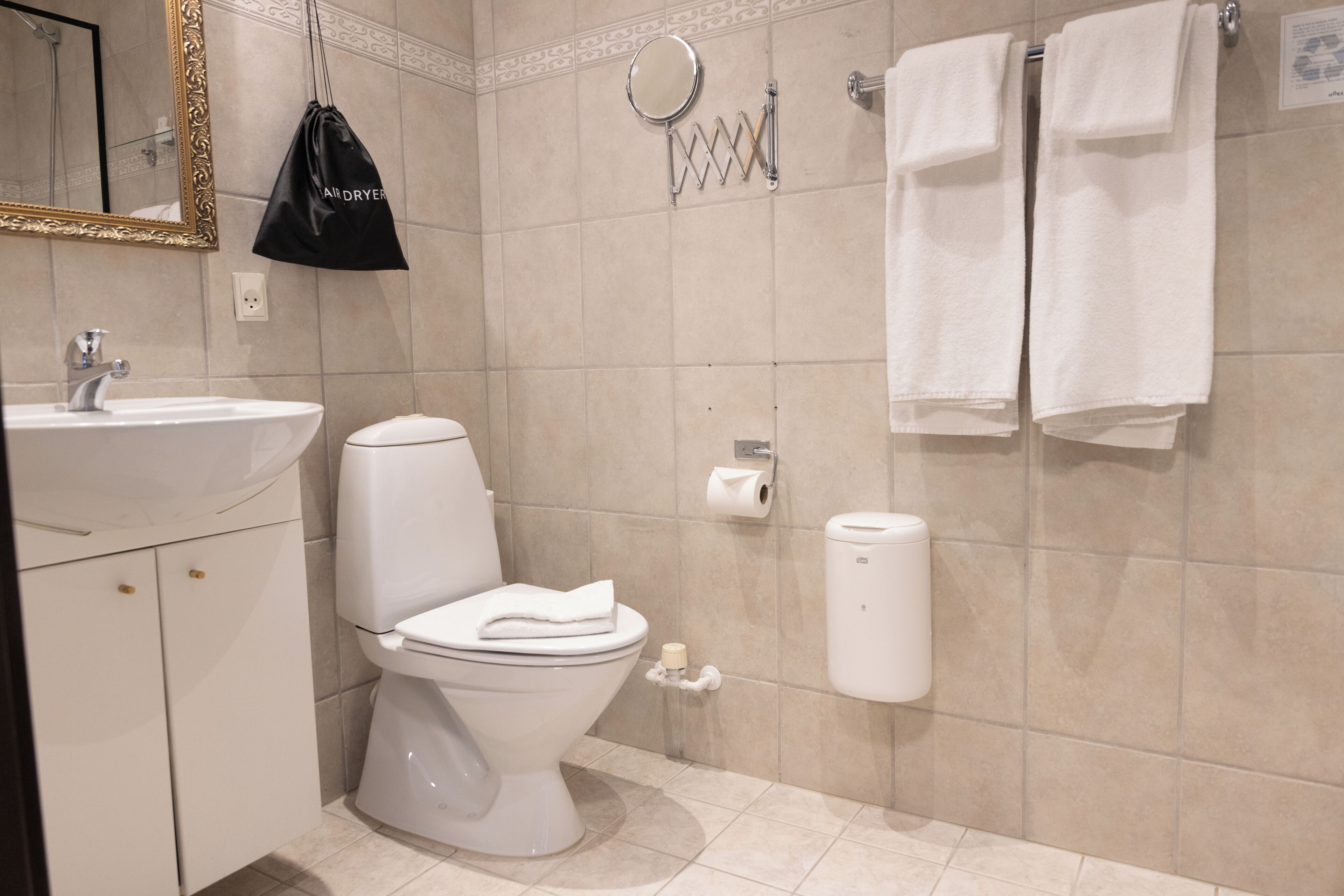 Une salle de bain équipée de toilettes, d’un lavabo, d’un porte-serviettes et d’un sac accroché au mur.