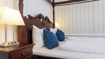 A four-poster bed with white linens, two blue pillows, and a wooden nightstand with a lamp.