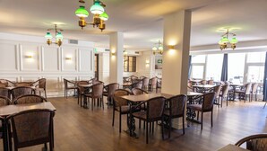A spacious dining area with multiple tables and chairs, elegant chandeliers, and large windows allowing natural light. - Hotel Phønix (Aalborg)