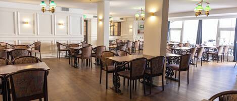 Un vaste espace dédié à la salle à manger, avec de nombreuses tables et chaises, de magnifiques lustres et de grandes fenêtres laissant entrer la lumière naturelle.