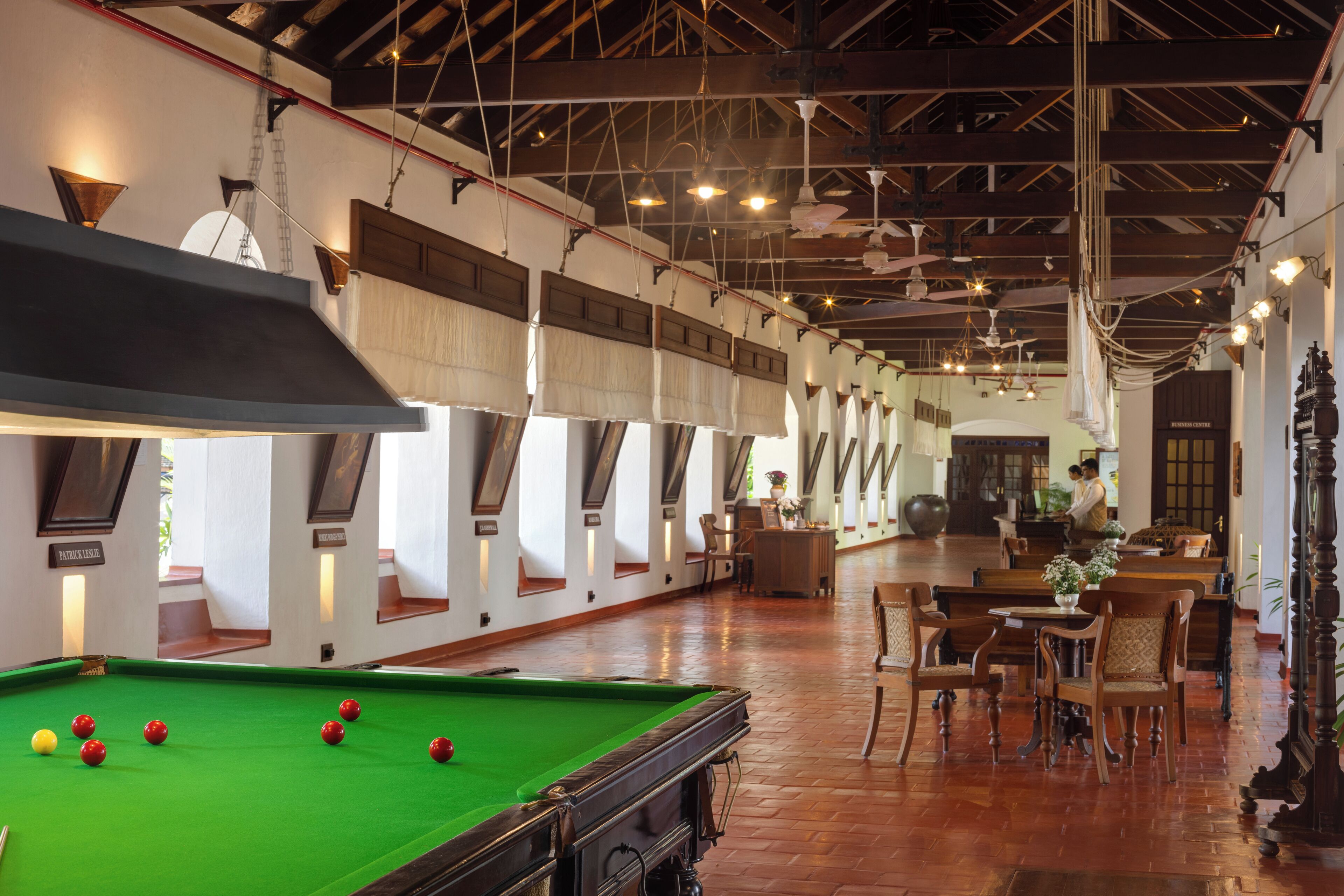 A billiards table with balls, wooden chairs, and tables in a room with high ceilings and exposed beams.