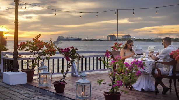 A couple dining at a table with a view of the water and sunset.
