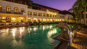 A hotel with a swimming pool, outdoor seating, and a well-lit facade.