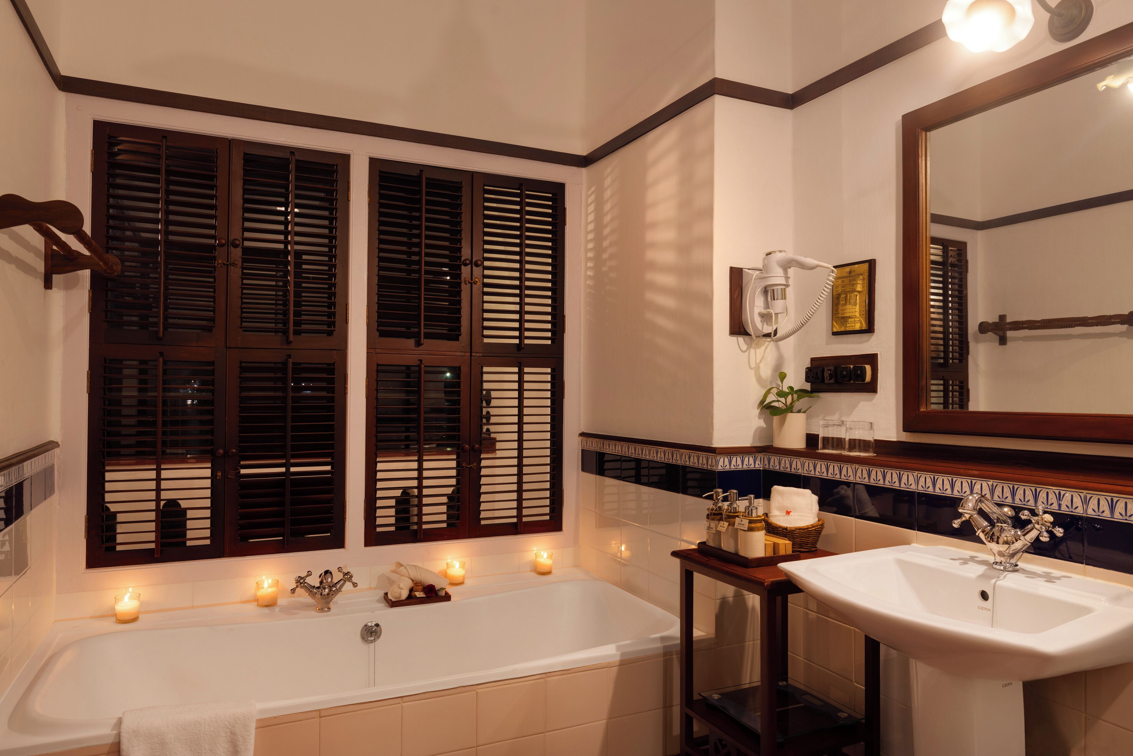 Un baño con bañera, lavabo, espejo y ventana con contraventanas.