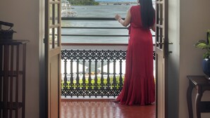 A woman in a red dress standing at an open doorway with a view of a body of water and a boat.