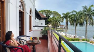 Relax on the balcony with a serene view of the calm water, surrounded by wicker chairs and a potted plant.