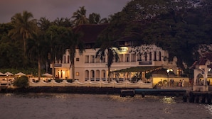 A waterfront hotel with a white facade, arched windows, and a balcony overlooking the water.