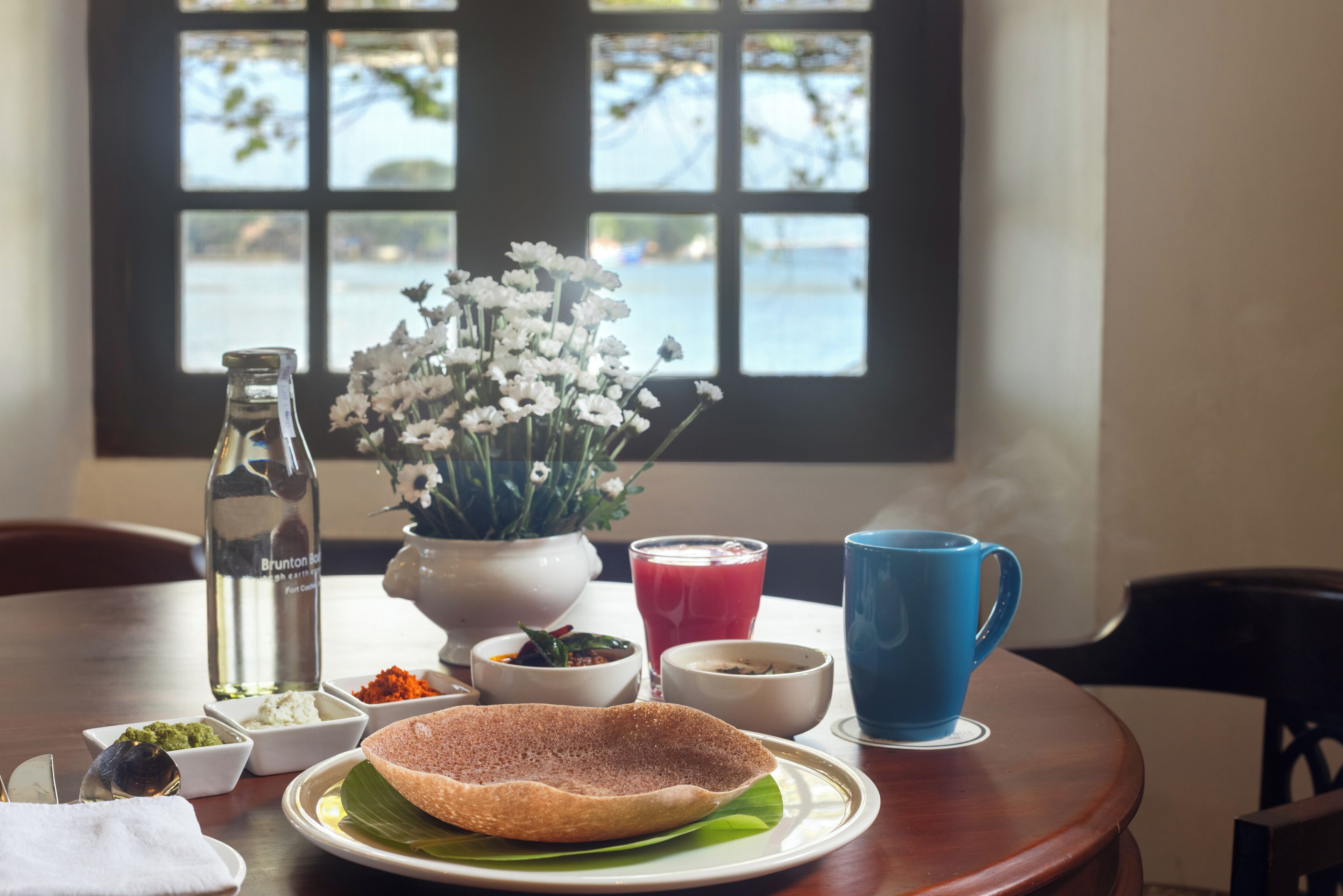 A table with a traditional meal, including a dosa, various condiments, and a blue cup.