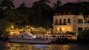 A boat docked at a waterfront property with a building featuring arched windows and a balcony.