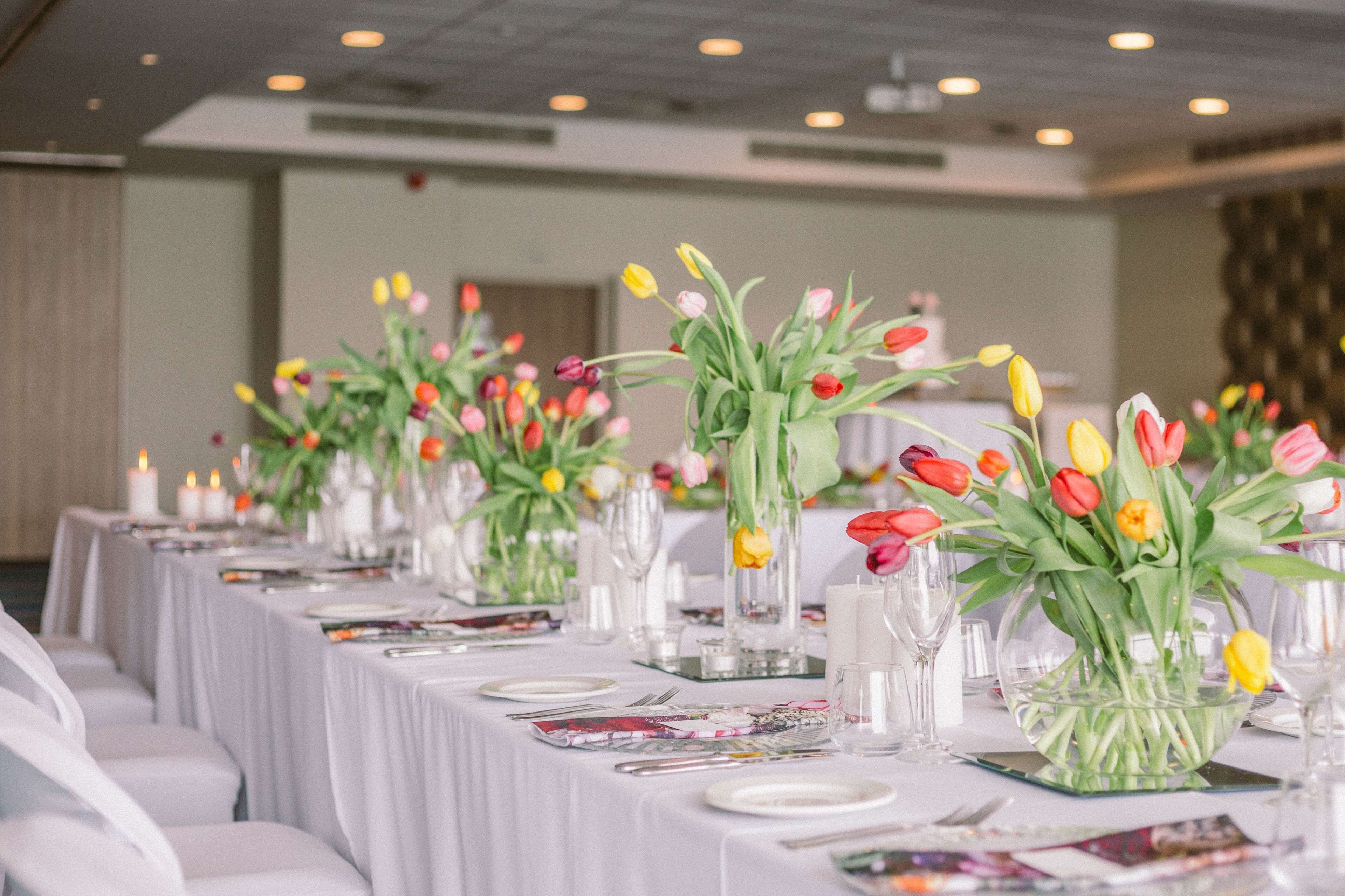 Une longue table dressée pour un événement formel, agrémentée de compositions florales et de bougies.