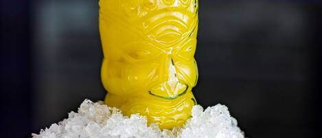 Et glas gul drik med is og et limeskive, placeret på en træunderkop med ekstra is.