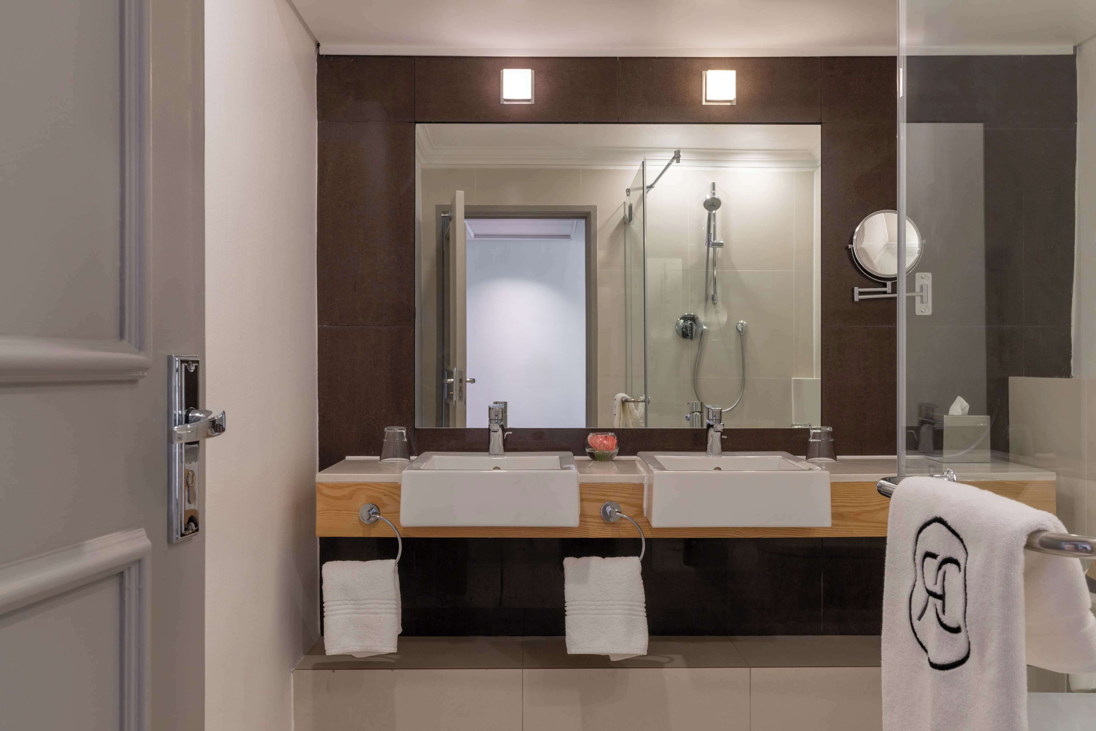 A modern bathroom with two sinks, a large mirror, and a glass shower enclosure.
