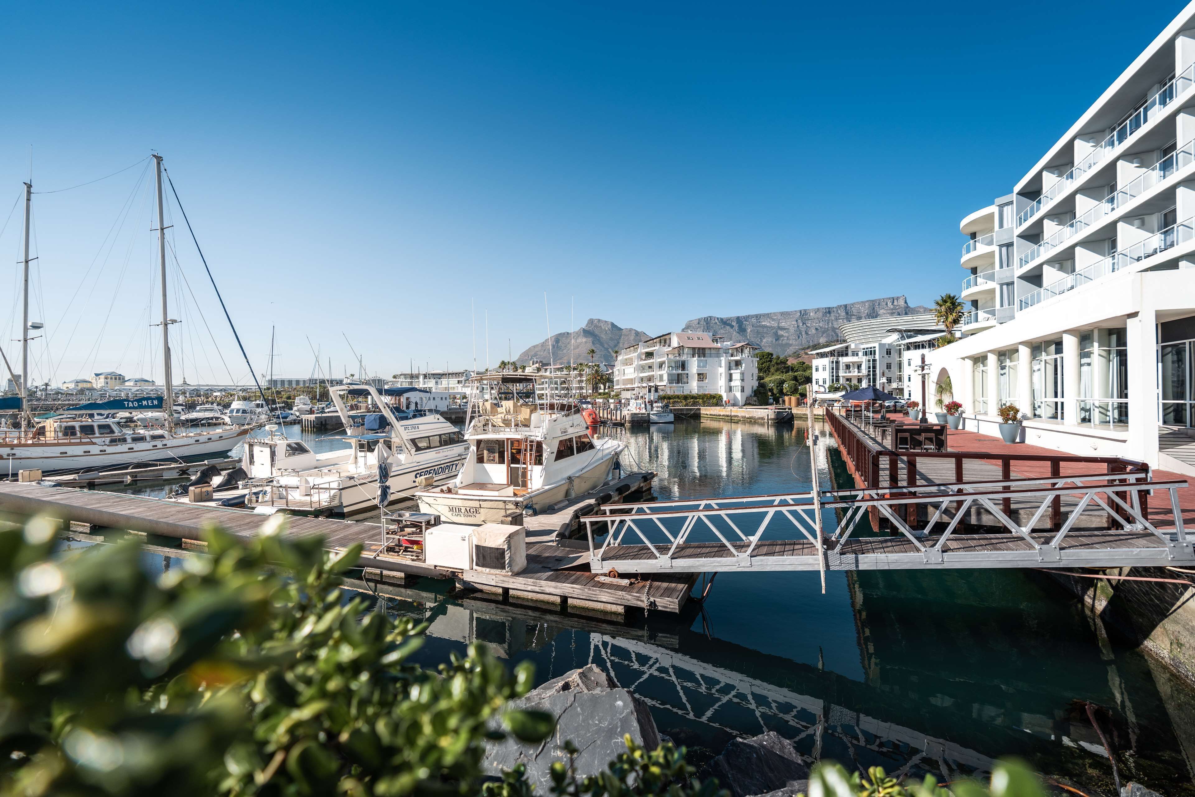 A marina with boats docked, a wooden pier, and a building with balconies.