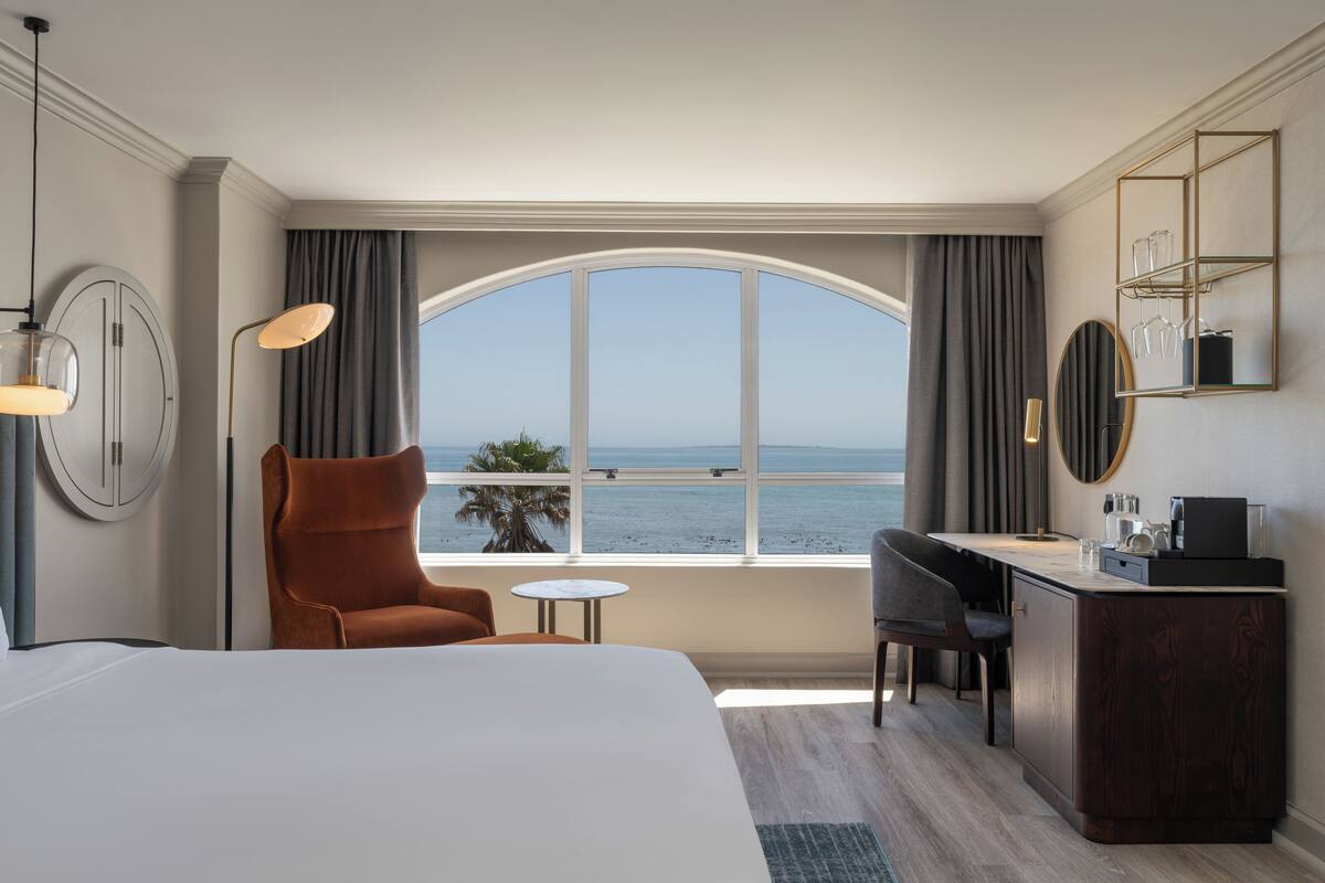 A hotel room with a large bed, a desk, a chair, and a view of the sea.