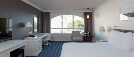 Habitación de hotel con una cama grande, un escritorio con silla, televisión y ventana con cortinas.