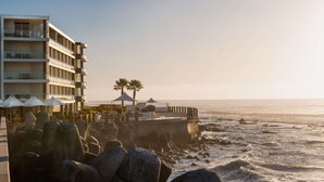 A beachfront hotel with multiple balconies, a pier, and umbrellas.