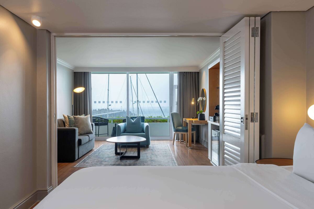A hotel room with a large bed, a sofa, a coffee table, and a view of a bridge.
