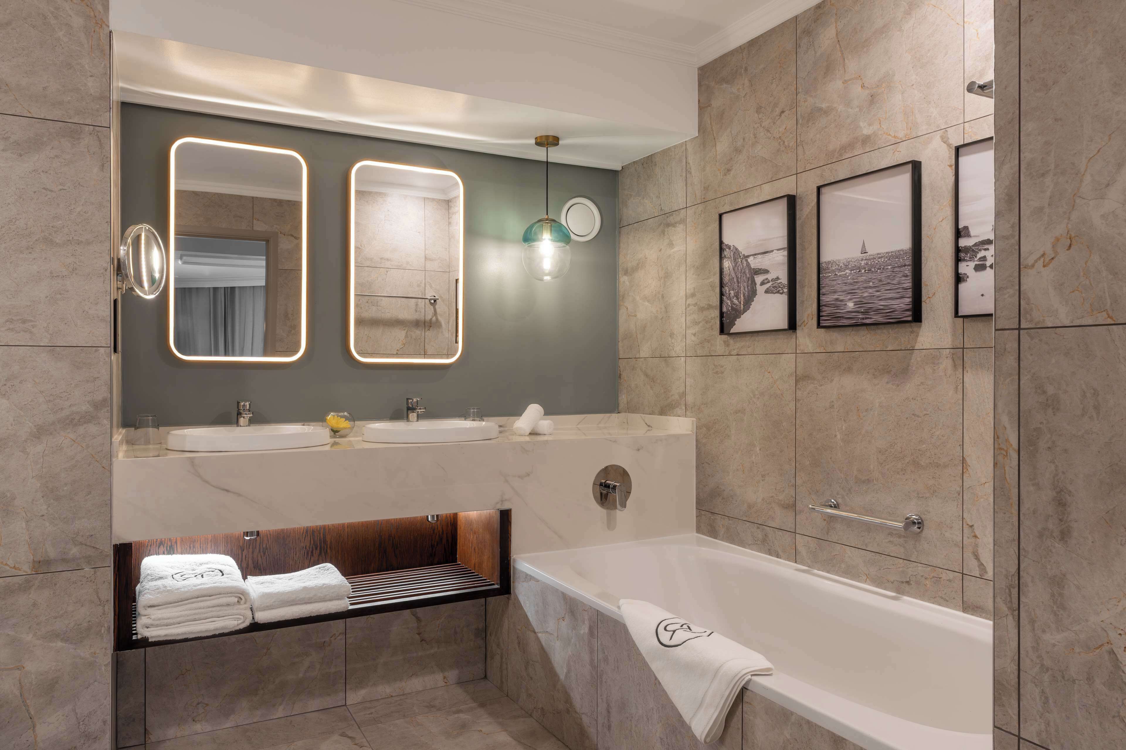 A modern bathroom with a bathtub, two mirrors, a vanity with a sink, and a towel rack.