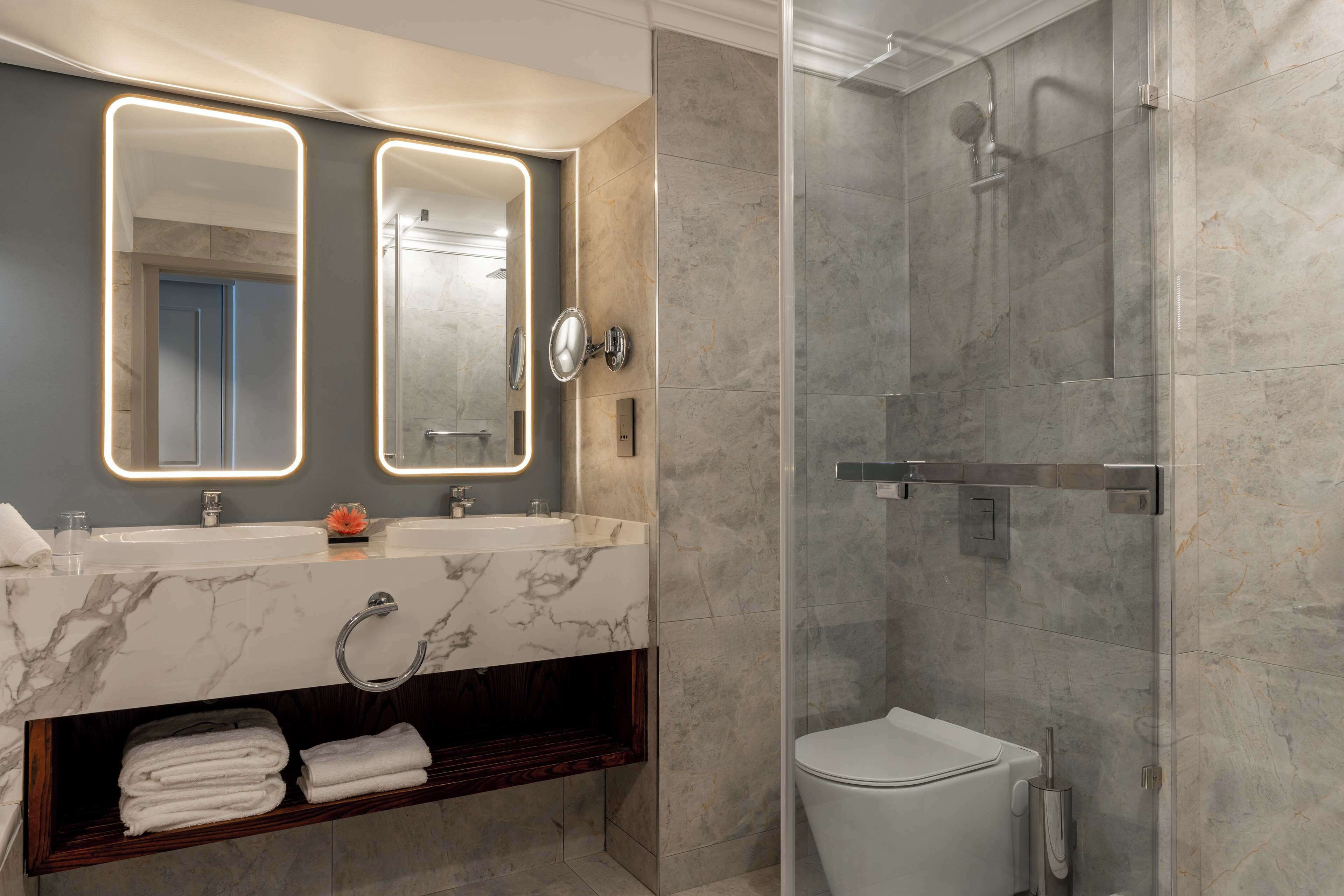 A modern bathroom with a marble vanity, dual mirrors, a glass-enclosed shower, and a toilet.