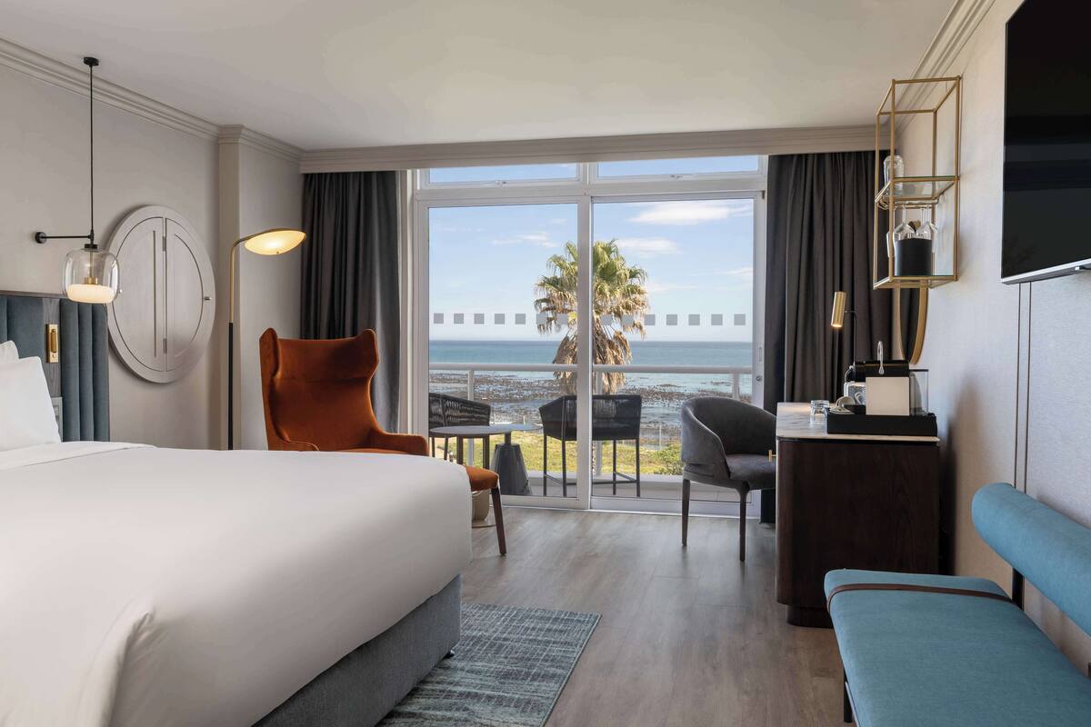 A hotel room with a large bed, a desk, a chair, and a view of the ocean.