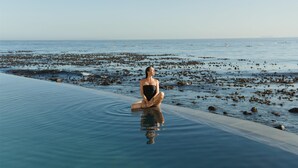 A person sitting in a clear pool with a view of the sea and rocks.