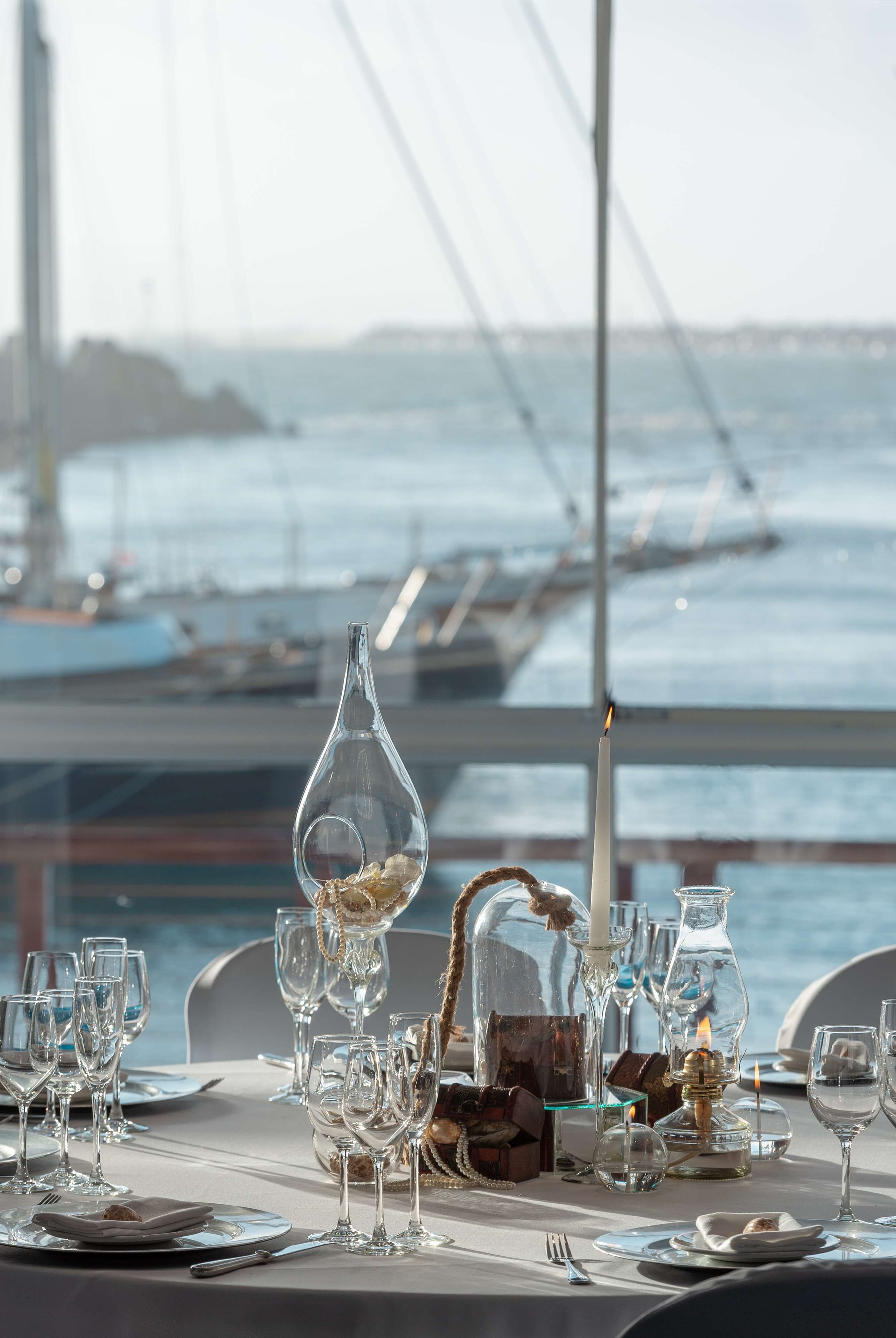 Une table dressée pour un repas, avec vue sur la mer et un pont en arrière-plan.