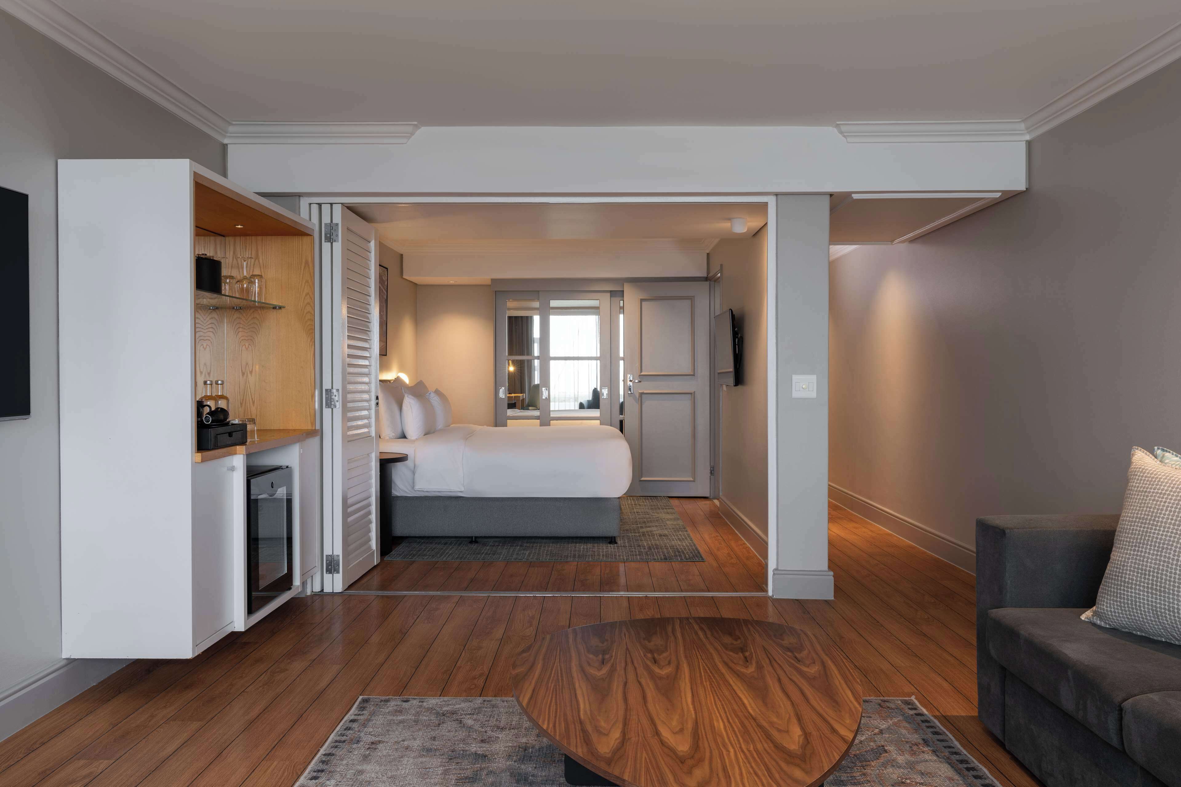 Una habitación de hotel moderna con una cama, un área de descanso con una mesita de centro y una kitchenette.